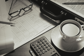 A professional workspace featuring a laptop displaying bookkeeping software, a calculator, financial documents, and a cup of coffee. The setting includes tropical elements that represent South Florida, such as palm leaves and bright lighting.